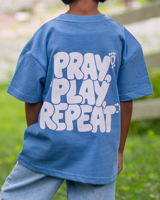 Child wearing a blue t-shirt with text, standing in a park-like setting.